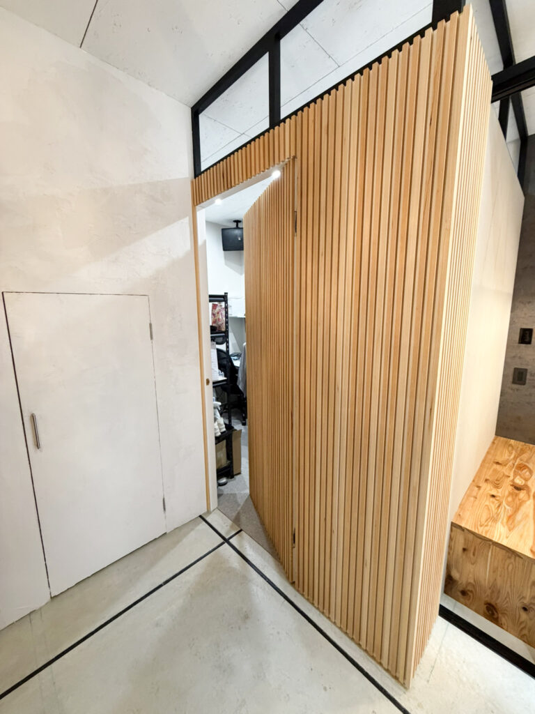 堺市西区の店舗リノベーション事例 造作のルーバー壁に設けた取っ手のない隠し扉(開いた状態)|TEAM-R